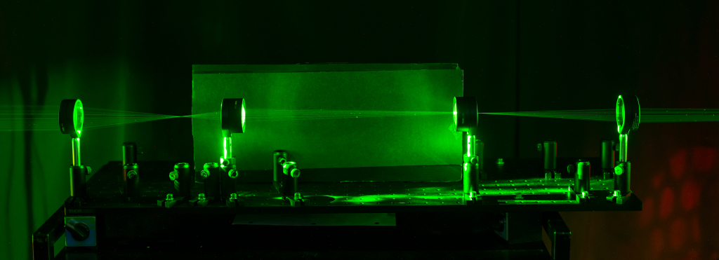 – An optical cloaking device that hides objects by taking advantage of the focal lengths of a set of lenses. The path light rays taken through the device is shown by shining a laser through the series of lenses. Picture courtesy of the University of Rochester.