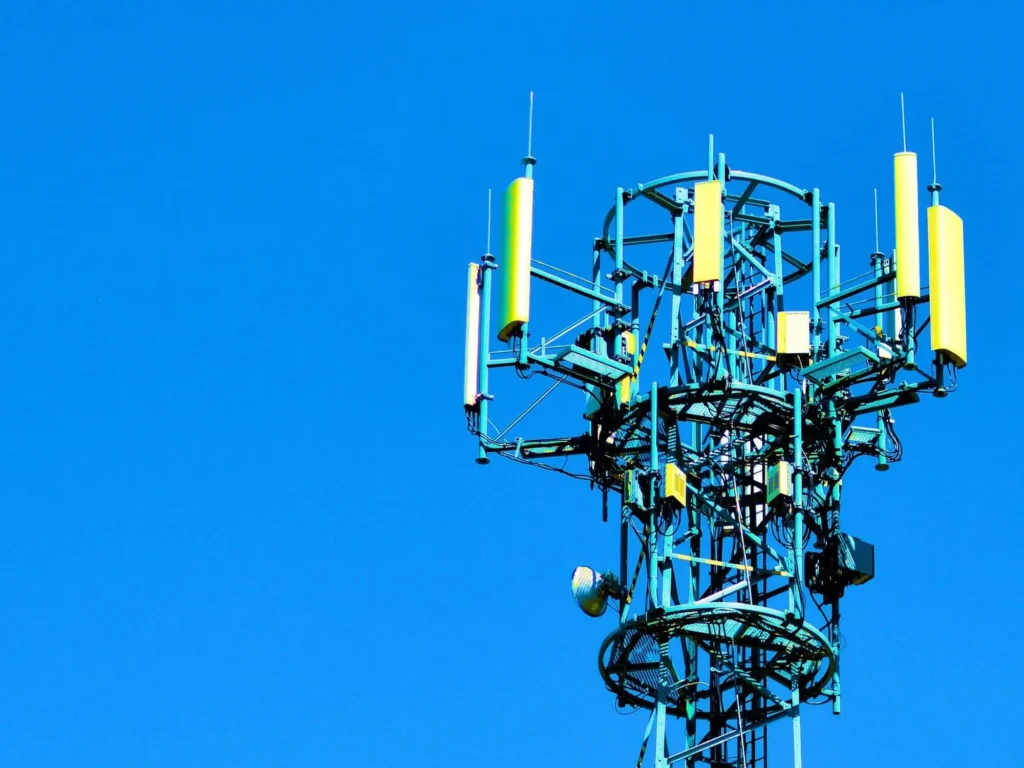 Image of a towering cell tower against a clear sky, equipped with various antennas and dishes for wireless communication.