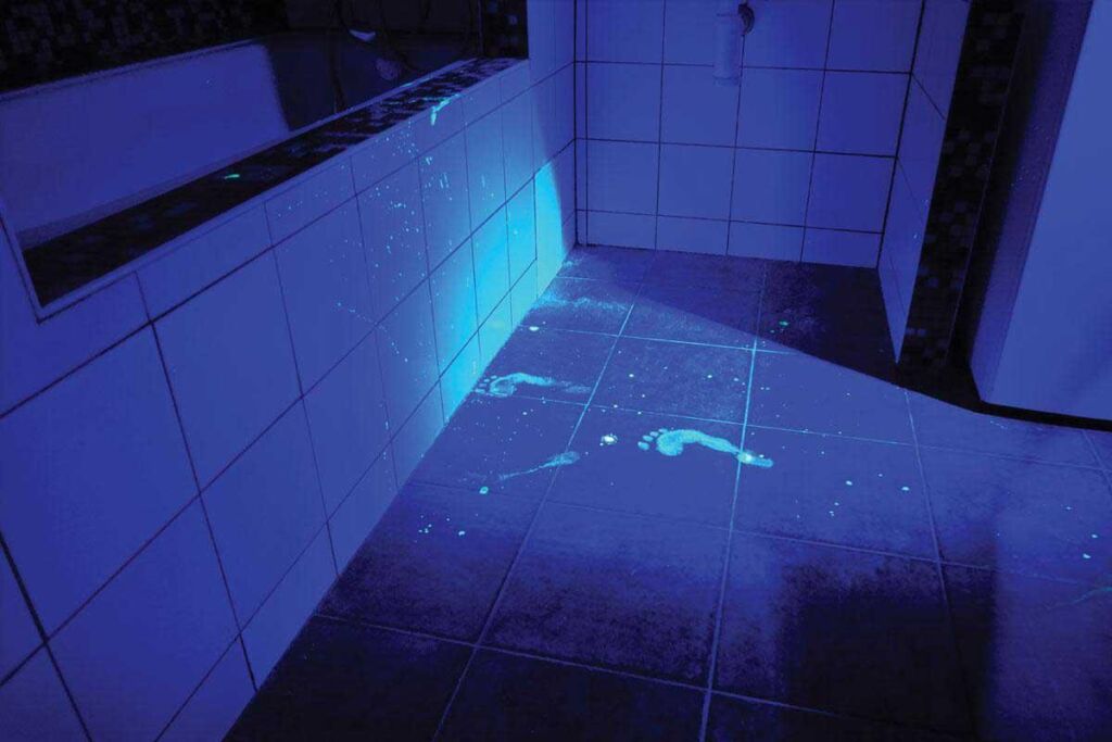 Image of a previously invisible footprint revealed on a dark surface under forensic UV light, showcasing the use of ultraviolet technology in crime scene investigation.