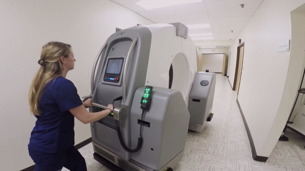 Photo of a nurse maneuvering a portable CT scanner through a hospital corridor, highlighting its mobility and accessibility.