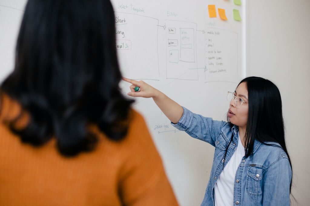 Storytelling in High-Tech Sales: Two women in a business meeting, with one explaining a concept on a whiteboard.